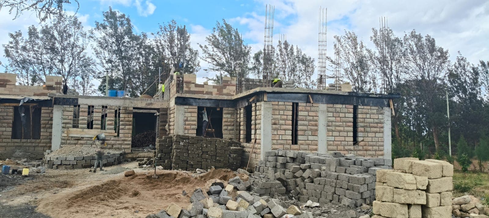 House walls rising with rebar starter columns and workers