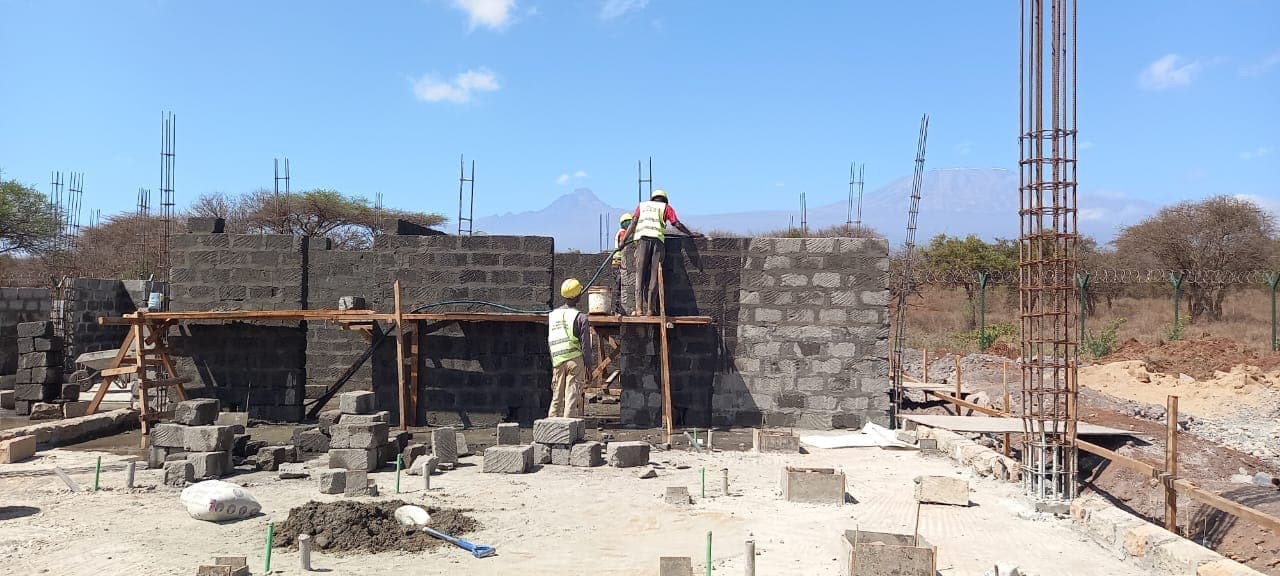 Masons building walls on site with Mount Kilimanjaro in the distance
